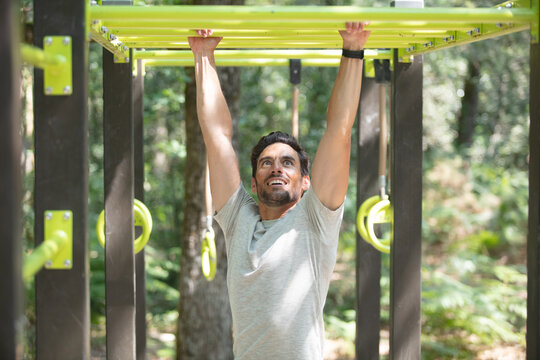 athletic brunette man pressed on parallel bars at street gym