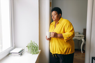 Sad upset lonely plus size elderly retired female of african american ethnicity standing in front...