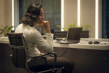 Side view of young businessman sitting at desk in office and looking away, Business disappointment...