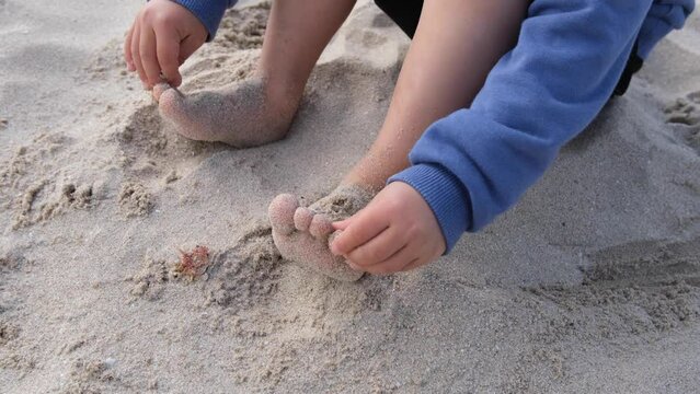Close up of bare feet of an unidentified young Asian boy (3 to 4 years old) playing sands alone on the beach. Concept of free childhood fun, family-friendly vacation, and relaxing summer playtime.