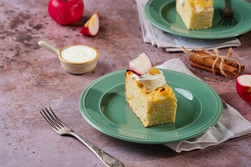 Sliced kugel, casserole of noodles, cottage cheese, apples and raisins on a green plate on a brown concrete background. Jewish cuisine. Noodle dishes.