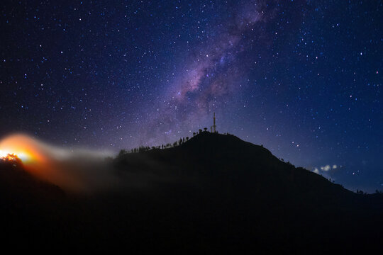 Communication mobile phone tower on peak of mountain standing out with clouds fog rolling over hills with lights of city in distance