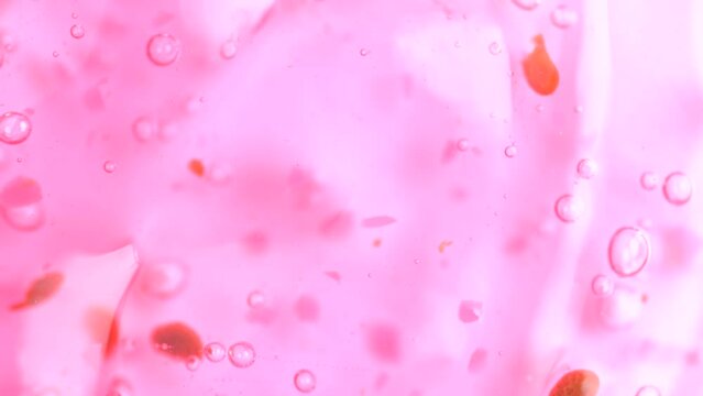 Liquid transparent pink cosmetics product with bubbles macro, top view.  Pink shower gel rotation. Slow Motion. Peeling gel with raspberry. Exfoliating shower gel, scrub with raspberry seeds