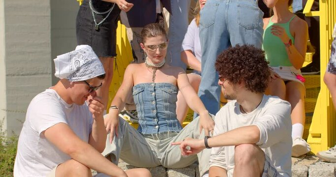 Students gather to enjoy music and dance freely in an open space on campus. The girl laughs loudly in communication with two guys. Polyamorous relationships at the development stage. Youth portraits.
