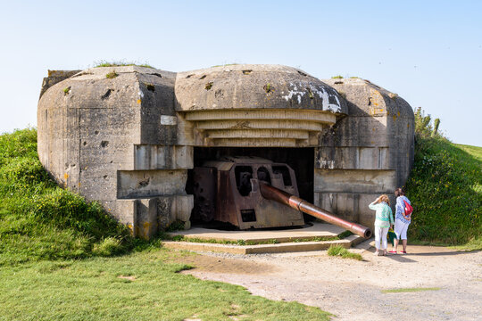 Two tourists observe the 150 mm gun in a bunker in the Longues-sur-Mer battery in Normandy, France, a WWII German coastal artillery battery part of the Atlantic Wall fortifications.