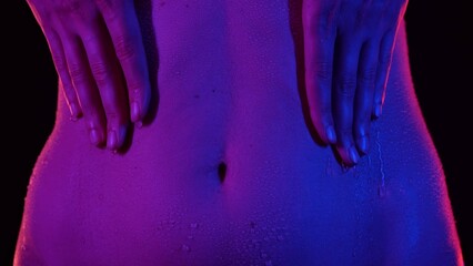 Closeup shot of beautiful caucasian woman body part in neon light, touching belly area skin in...