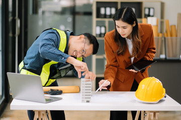 Contractor and architect looking at plan, tablet, laptop and talking about working on big project. Building in construction office interior.