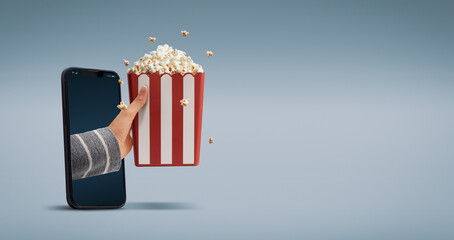 Hand holding popcorn coming out of a smartphone screen