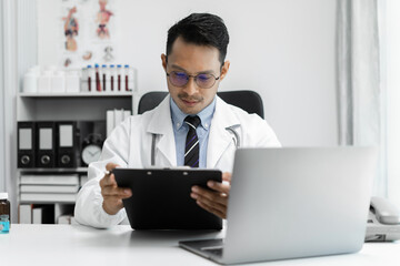 Doctor working on laptop computer, writing prescription clipboard with record information paper...