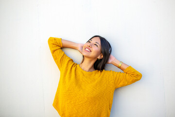 smiling young woman leaning against white wall with hands behind head