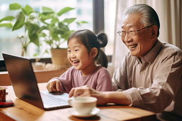 Asian grandfather and granddaughter talking on video conference, looking at laptop