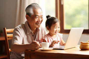 Asian grandfather and granddaughter looking at laptop and drinking tea