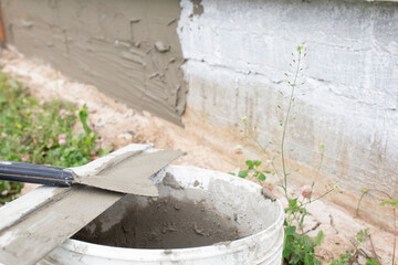 Bucket with spatula and cement plaster. Coating the foundation of a house with concrete mortar. I