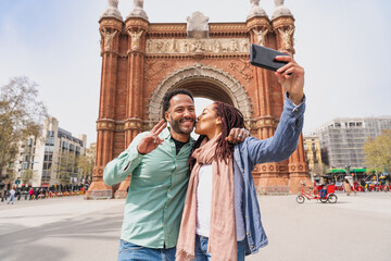 Beautiful happy hispanic latino couple of lovers dating outdoors - Tourists in Barcelona having fun during summer vacation and visiting Arc de Triumf historic landmark - obrazy, fototapety, plakaty