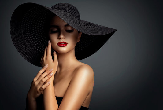 Fashion Woman in Black Wide brim Hat with Red Lips Makeup. Mysterious Elegant Lady Portrait over Gray. Beautiful Model with Perfect Make up and Hands Manicure