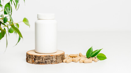 Supplement bottle mock up on wooden podium with herbal pills and green leaves or vitamins on white background with copy space, organic medication. Natural herbal supplement