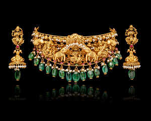 A beautiful golden Necklace and Earrings with green emerald stones and diamonds, on a black...