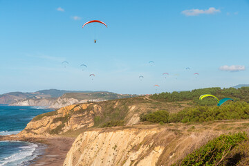 Paragliders flying over the sea coast with blue water, sandy beach and cliffs in sunny day. Paragliding on the Sopelana beach near Bilbao, Basque country, Spain. Popular place for extreme sport