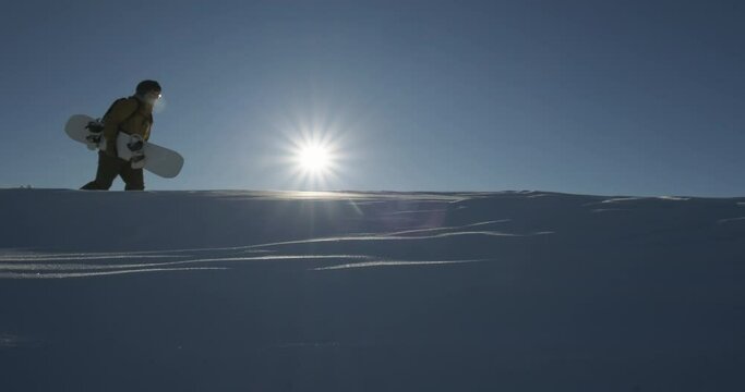 Snowboarder freerider walking up climbing the mountain ridge. Extreme freeride snowboarding down the mountain slope. Active lifestyle, adventure, winter sport concept. Slow motion