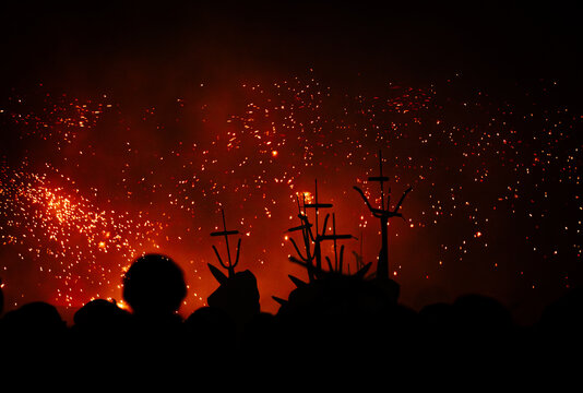 Silhouettes of people and devils with torches from the pyrotechnic show and fireworks of the devils and Correfocs on a street in Granollers at night during the traditional festival.