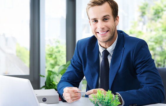 Portrait photo - business man at workplace table near window background. Happy smile confident businessman in suit with laptop computer. Business lawyer, bank consulting, trade broker