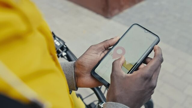 Over shoulder shot of hands of food delivery man checking map on his phone