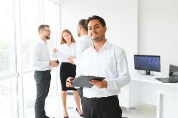 Portrait of smiling indian businessman standing in modern office on colleagues background