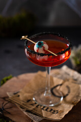 Halloweens spooky drink red martini cocktail. Bloody martini garnished with jelly eye on scary dark background with spiderweb, moos and spiders. Festive drink for vampire party. Close up