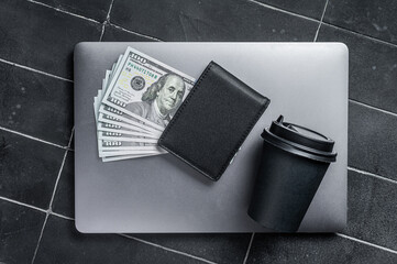 Corporate business desktop with laptop, digital tablet, wallet, money and cup of coffee. Black background. Top view. Copy space