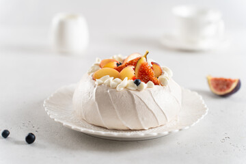 Pavlova cake with meringue, peach, figs, blueberries and vanilla whipped cream on a white background. Side view, close up. Summer meringue dessert recipe, menu. Confectionery, cooking courses