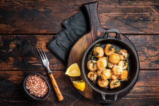 Scallops seared in garlic, thyme and butter served in cast iron skillet. Wooden background. Top view