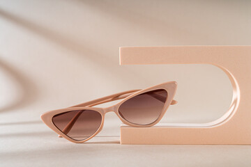 Trendy beige cat eye frame sunglasses on a podium on a beige background. Women's stylish sunglasses...