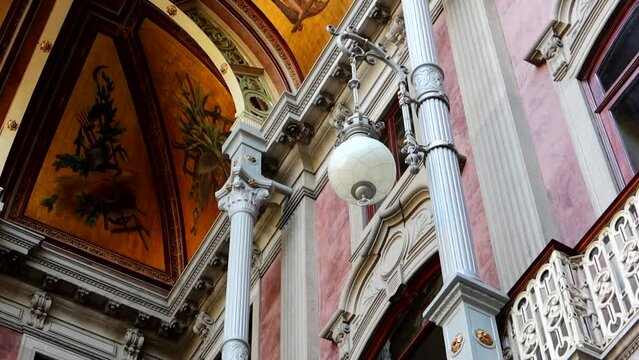 White lamp hanging on wall of Palacio da Bolsa in Porto with ornate ceiling in background. Low angle