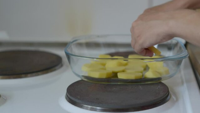 Close up shot of a woman placing potatoes in a glass baking tray, in a small kitchen during summer midday. Panasonic Lumix S5 with a 75mm lens.