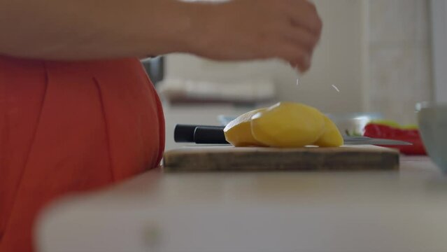 Trucking shot of a woman placing peeled potatoes on a cutting board. Panasonic Lumix S5 with a 75mm lens.