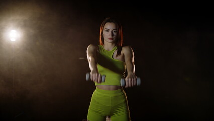 Sport woman training with dumbbells in slow motion. Back view of fitness girl exercising with weight dumbbells on black background. Strong model sport workout with dumbbell. Weight lifting concept