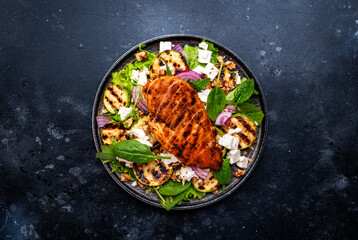 Gourmet salad with zucchini and grilled chicken, feta cheese, walnut, onion and spinach, black table background, top view