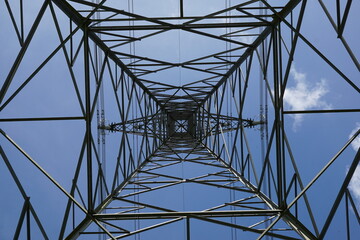 Symmetrical shapes of electricity pylon tower against blue sky background. Power and energy infrastructure  
