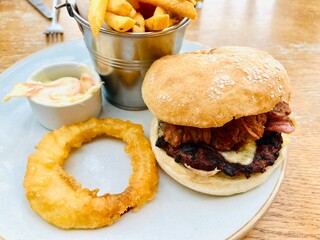 Beef burger in a white bread roll with French fries, onion ring and coleslaw served on a white plate