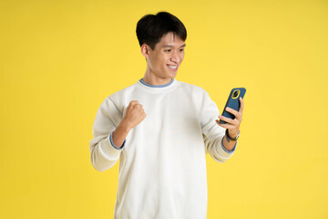 portrait of young Asian man wearing sweater and using phone on yellow background