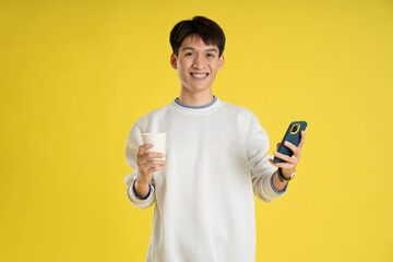 portrait of young Asian man wearing sweater and using phone on yellow background