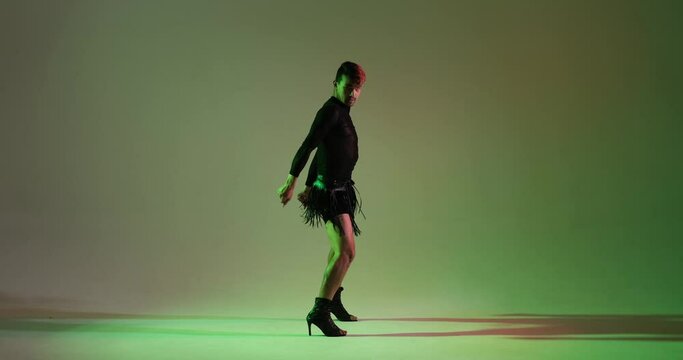A man confidently dances in high heels on a vibrant green background. His stylish and poised moves create a visually captivating and unique performance, highlighting his boldness and dance talent.
