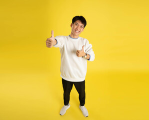 full body of young Asian man wearing sweater and posing on yellow background