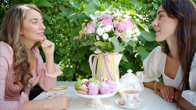 Women talking at a tabale with composition with flowers, macaroons sweets desert and coffee and tea