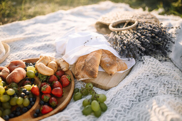 Picnic at sunset. Freshly baked bread with croissants, strawberries, grapes and peaches and a basket of fresh lavender
