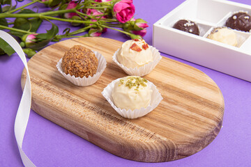 Three cheese truffles on wooden tray on purple background. Natural chocolate candies