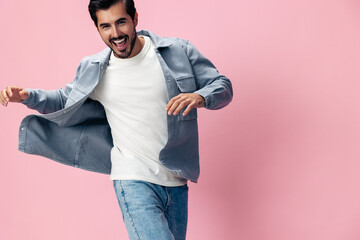 Fashion brunette man with beard happiness open mouth jumping and running with his arms spread on a pink background in a white T-shirt and jeans smile and joyful emotion on his face, copy space