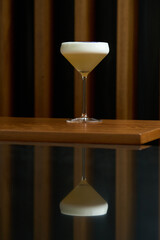Cocktail glass with white froth and purple flower petal.