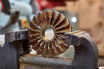 Worn out dirty bronze impeller from centrifugal pump in vice grip jaws. © Igor Hotinsky