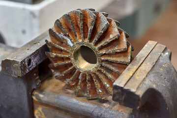 Close up of worn out bronze impeller from centrifugal pump in vice grip jaws.